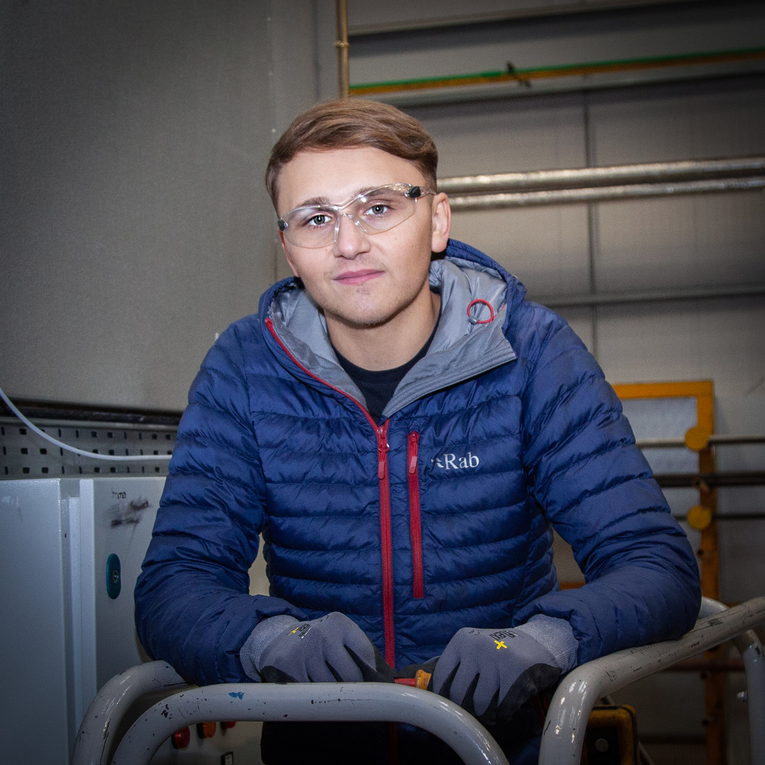 Electrical apprentice stood in front of a boiler smiling at the camera